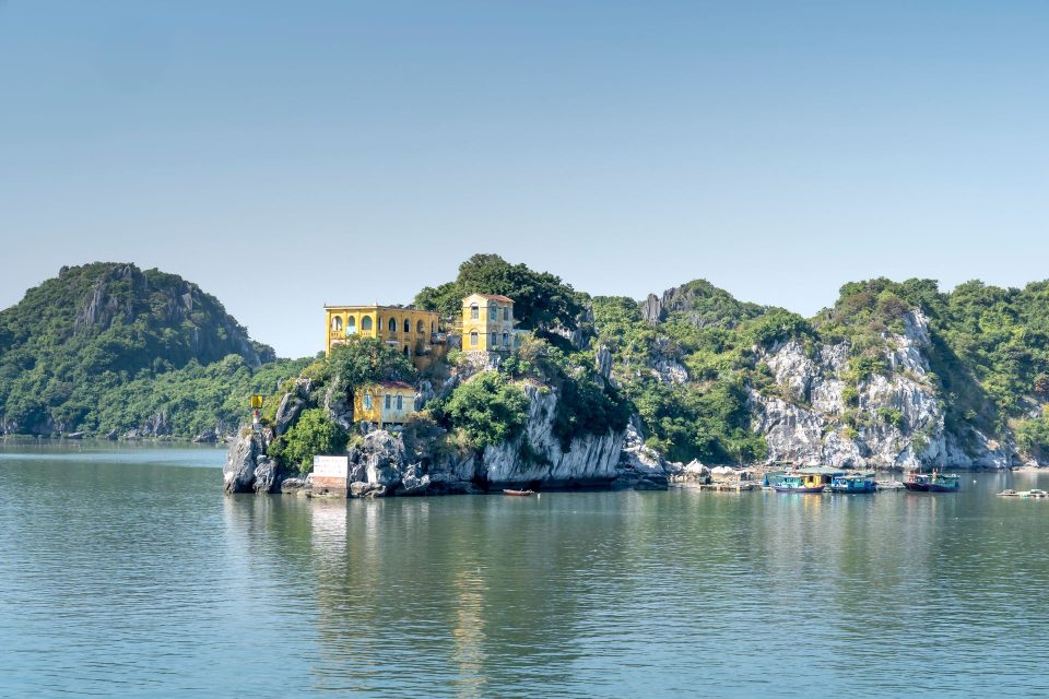 Island villa perched on rocky cliffs of Cat Ba, Vietnam with calm sea and surrounding foliage.