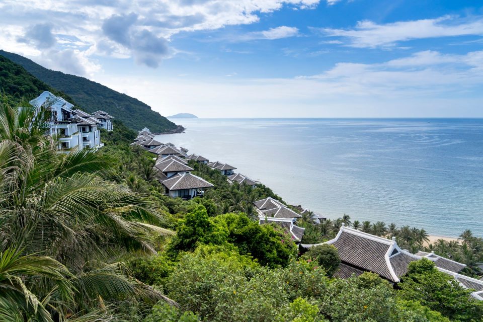 A serene tropical resort by the ocean with lush greenery and traditional villas under a clear blue sky.