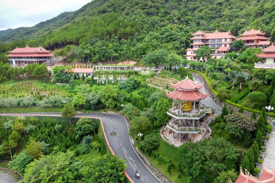 A scenic aerial shot showcasing a Vietnamese temple complex surrounded by lush green hills and forests.