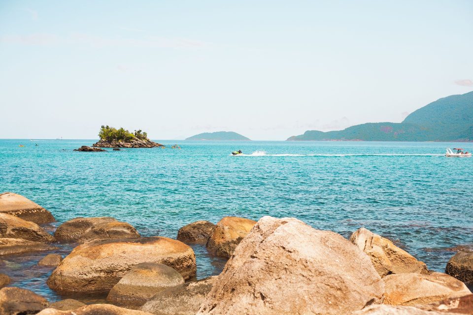 A tranquil seascape featuring rocky shorelines and distant islands under a clear blue sky.