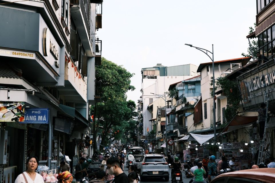 Busy street view in Hanoi, featuring people, shops, and vehicles, capturing the vibrant city life.