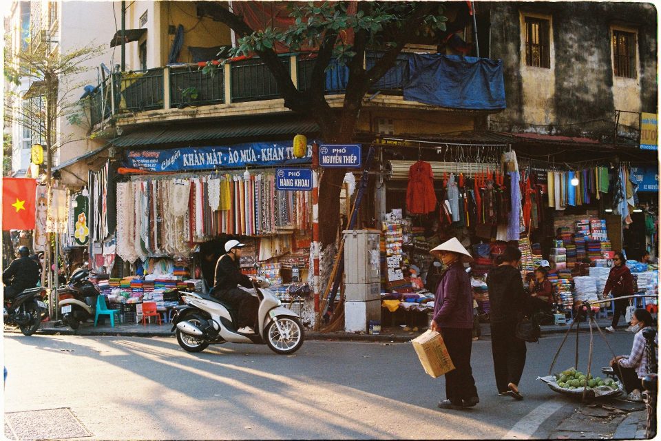 Vibrant street market in Hanoi, Vietnam with people and colorful fabrics.