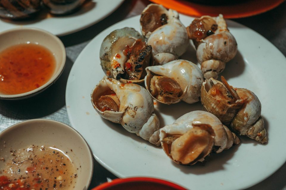 Delicious cooked sea snails served on a plate with dipping sauces, ideal for Asian seafood cuisine concepts.