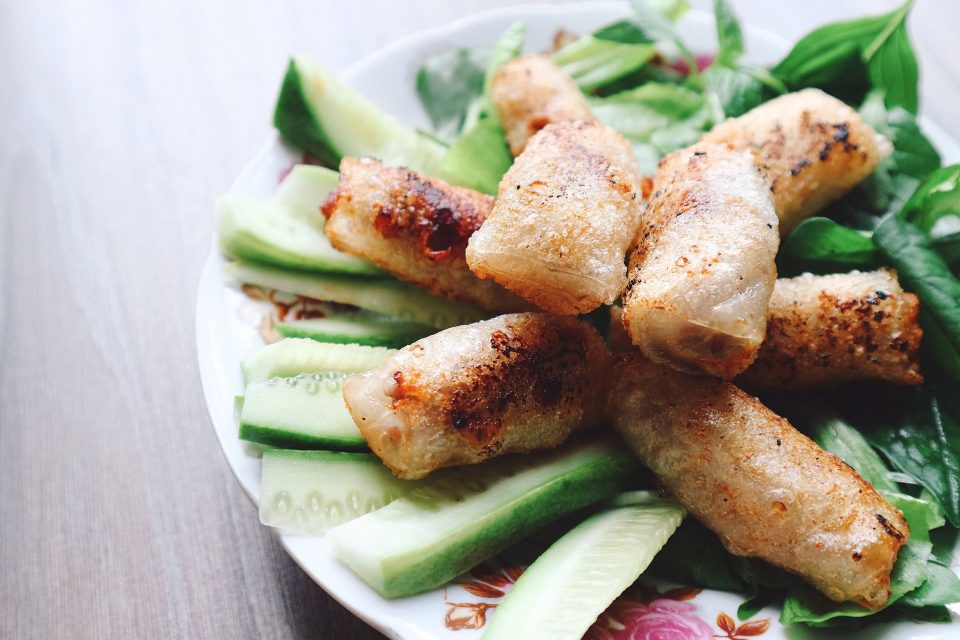 Crispy spring rolls served with fresh cucumber and herbs on a plate.