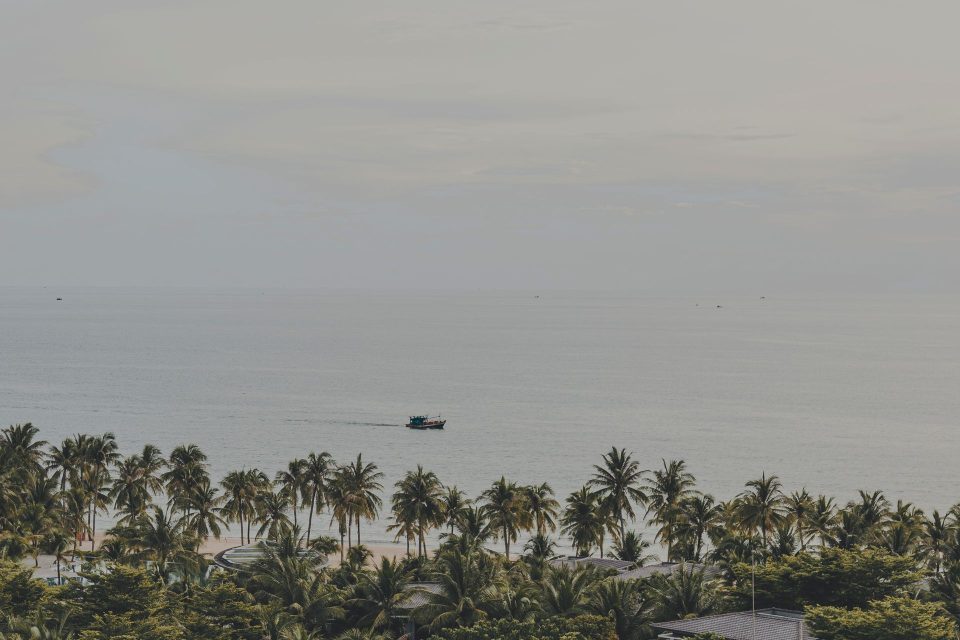 Serene panorama of palm-lined Phu Quoc beach with a distant boat on the calm sea.