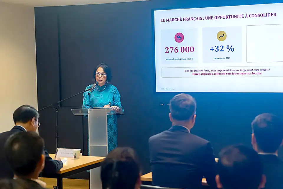 TS Lê Y Linh mặc áo dài xanh đứng tại bục phát biểu; màn hình phía sau ghi 276 000 du khách Pháp đến Hà Nội năm 2025, tăng 32 % so với năm 2024