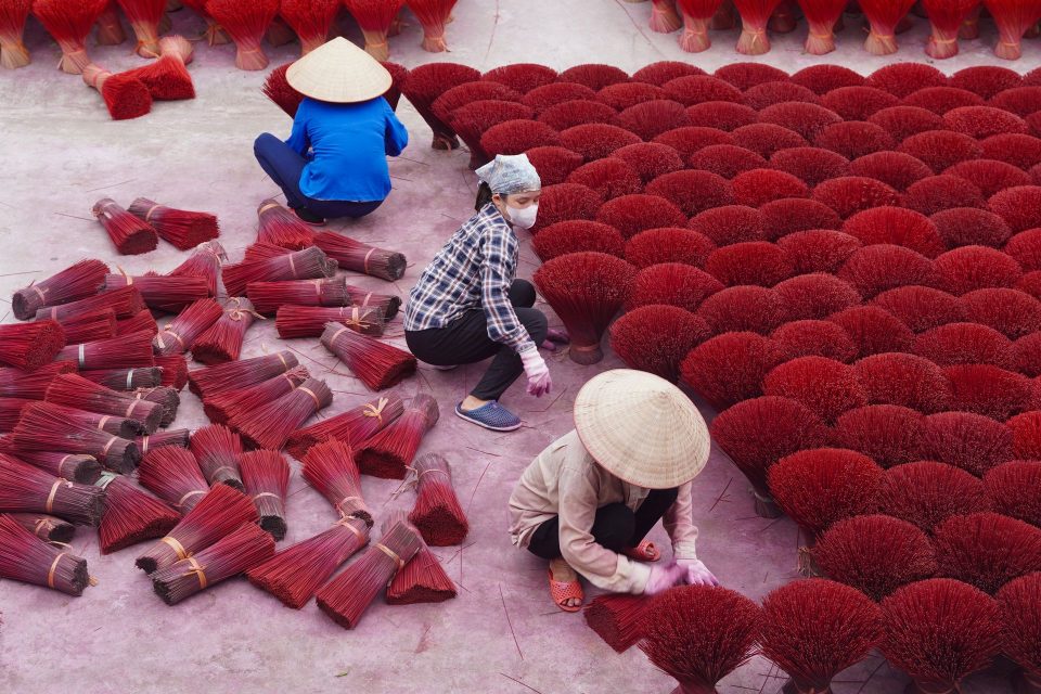 Artisans in Hanoi craft village arranging vibrant red incense sticks outdoors.