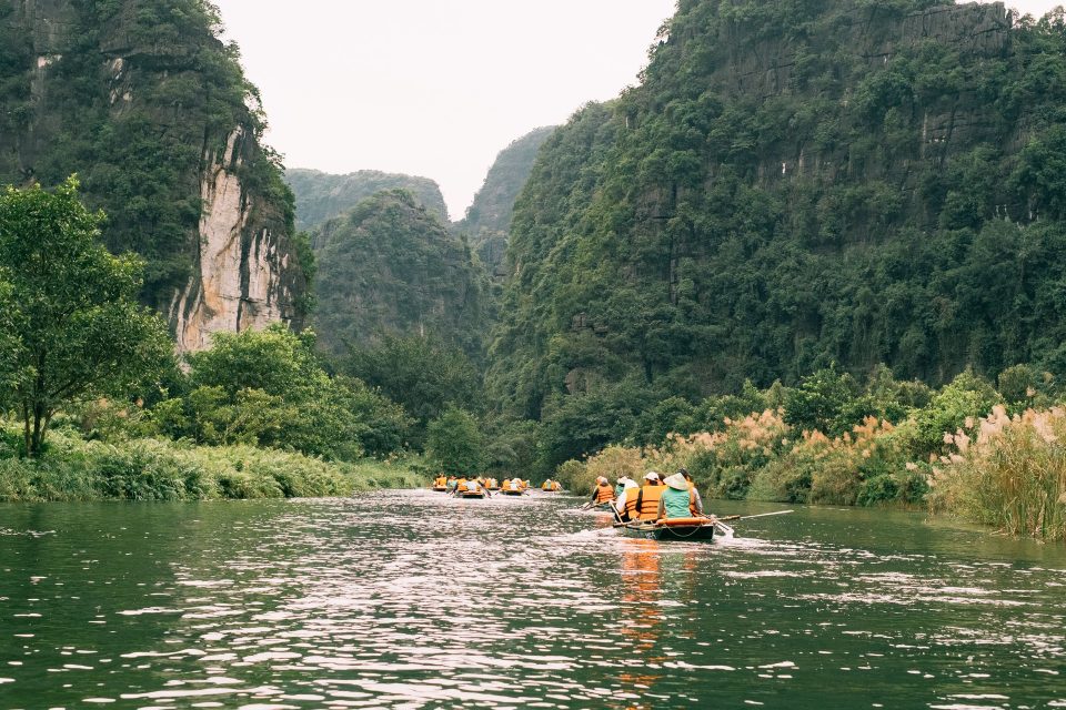 Group of kayakers paddling through a lush green valley surrounded by towering cliffs.