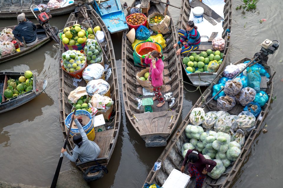 Aerial view of a bustling floating market with boats loaded with fresh fruit and vegetables.