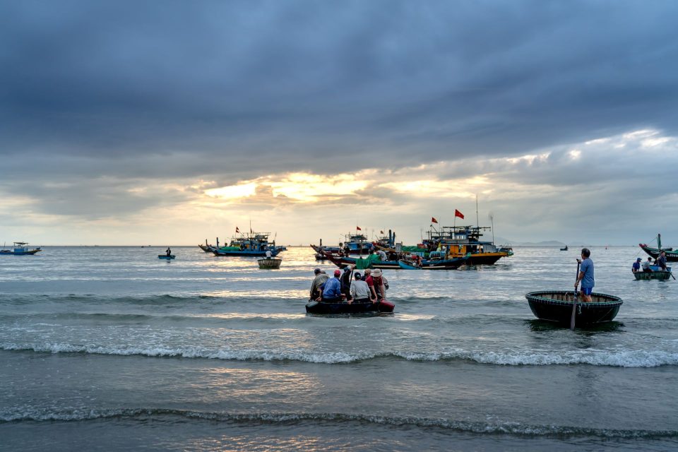 Fishermen navigating basket boats in the ocean with a cloudy sky at sunrise.