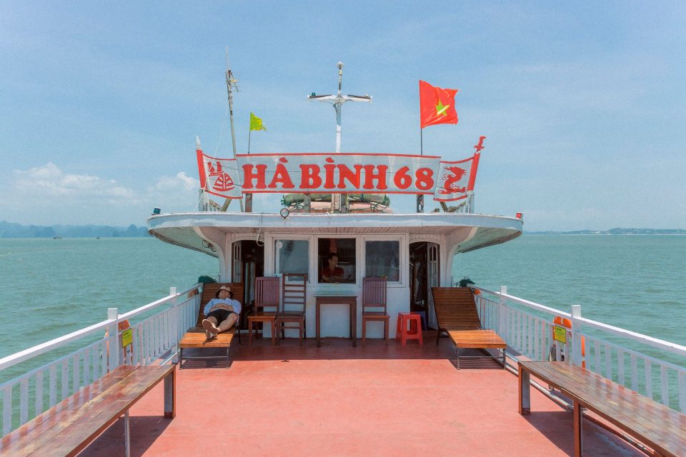 A man relaxes on a boat deck cruising through Halong Bay, Vietnam, under a clear blue sky.