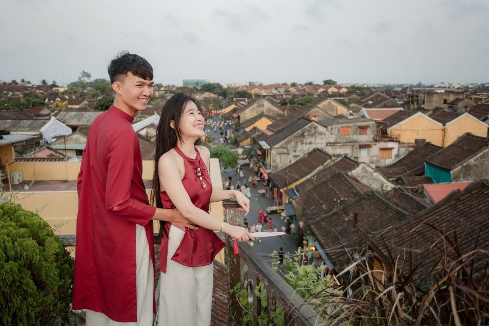 Couple in traditional outfits enjoying view of Hoi An roofs, showcasing Vietnamese culture.