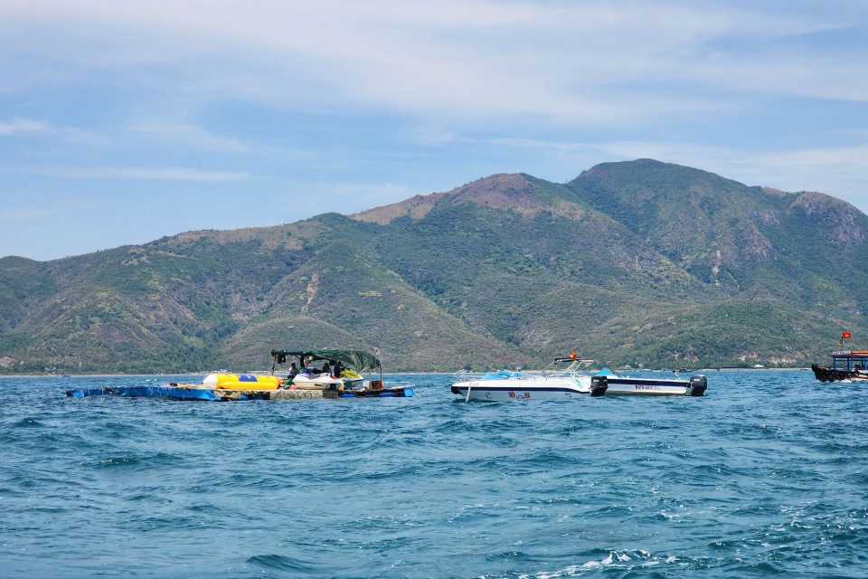 Blue waters and boats with scenic mountains in Nha Trang Bay, Vietnam, in the background.