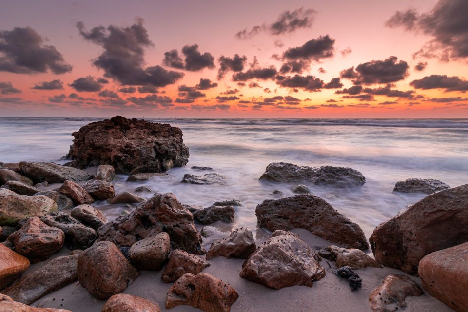 Peaceful sunset view over a rocky shoreline with vibrant sky and gentle waves.