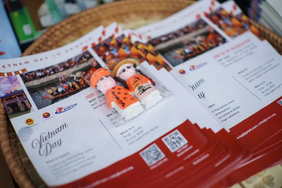 Tờ giới thiệu “Vietnam Day” xếp trong giỏ mây, bên trên là hai búp bê nhỏ mặc áo cam