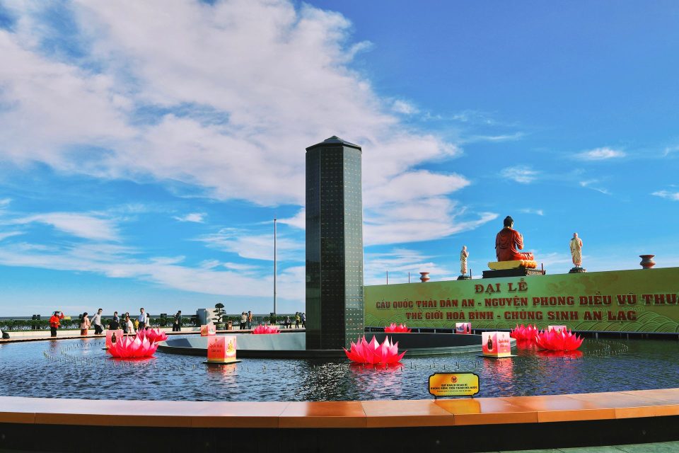 Colorful outdoor view of Ba Den Mountain with lotus pond and statues under a bright sky.