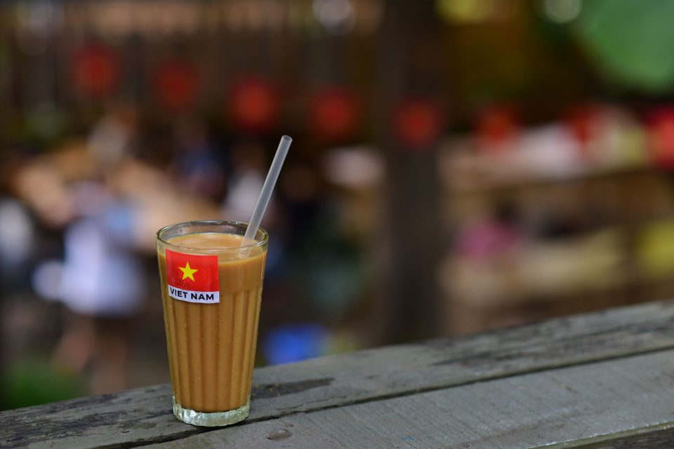 A glass of Vietnamese iced coffee with a Vietnam flag label, outdoors on a wooden surface.