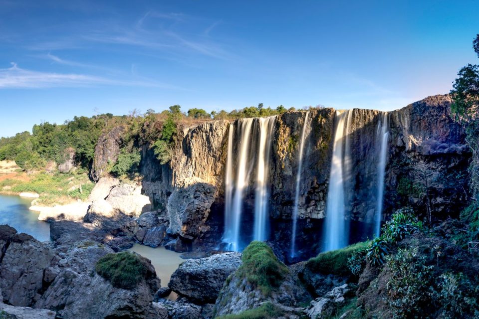 Breathtaking highland waterfall cascading into a serene lake under a blue sky.