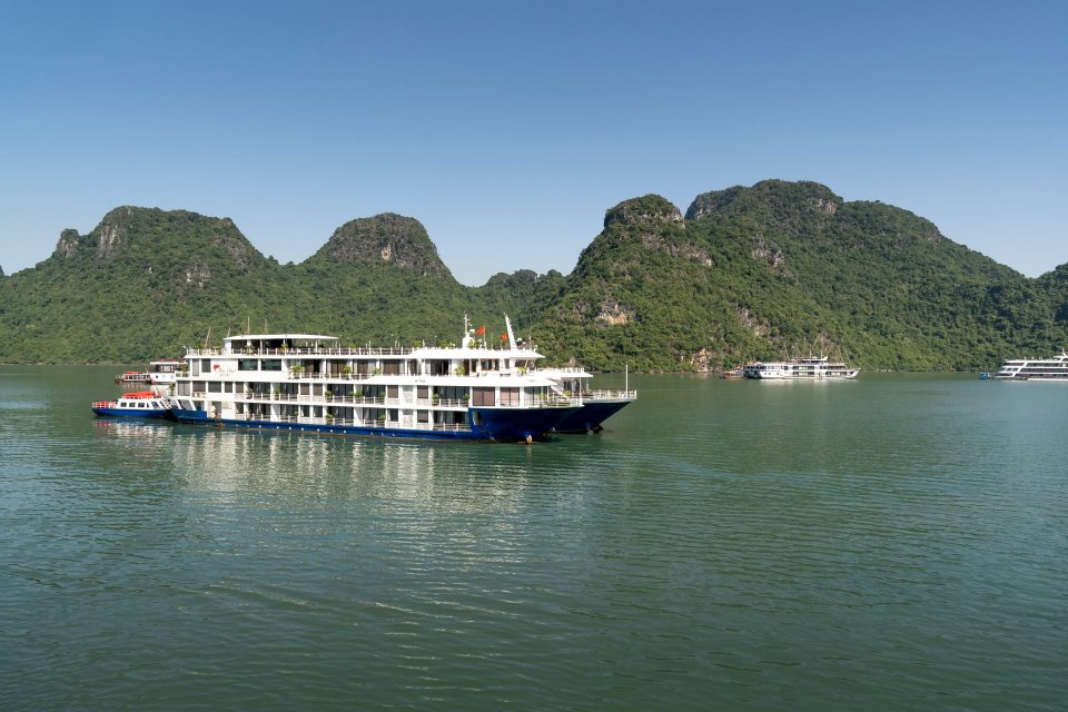 Beautiful cruise ships navigating the emerald waters of Halong Bay, Vietnam, surrounded by limestone mountains.