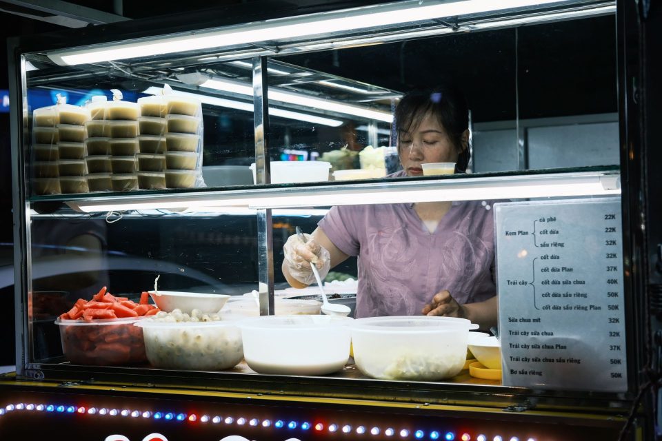 A street vendor prepares traditional Vietnamese desserts at an outdoor food stall at night.