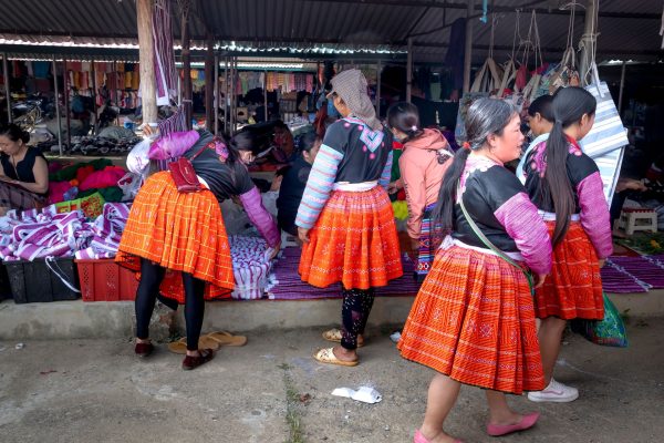 Women in vibrant traditional clothing shopping at a bustling market stall.